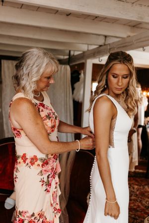 A tender moment during wedding preparations as final adjustments are made to a white dress.