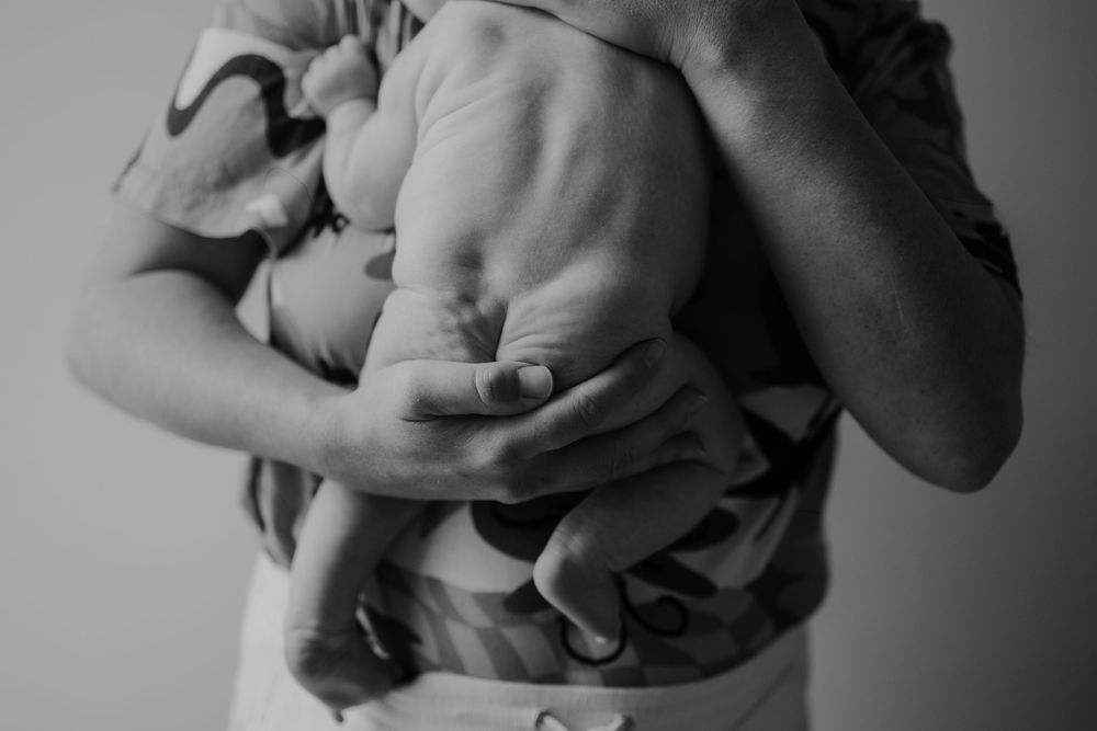 Black and white close-up of a parent tenderly holding a newborn baby against their chest.