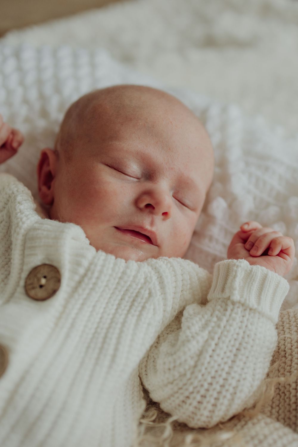 Close-up of a sleeping newborn in a white knitted sweater with wooden buttons.