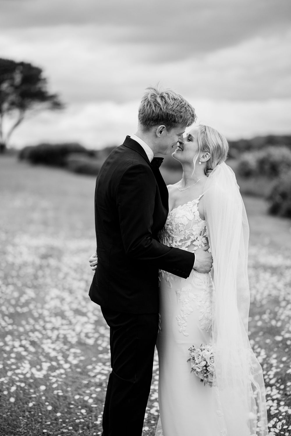 Black and white photo of a bride and groom sharing a kiss in a flower field on their wedding day.