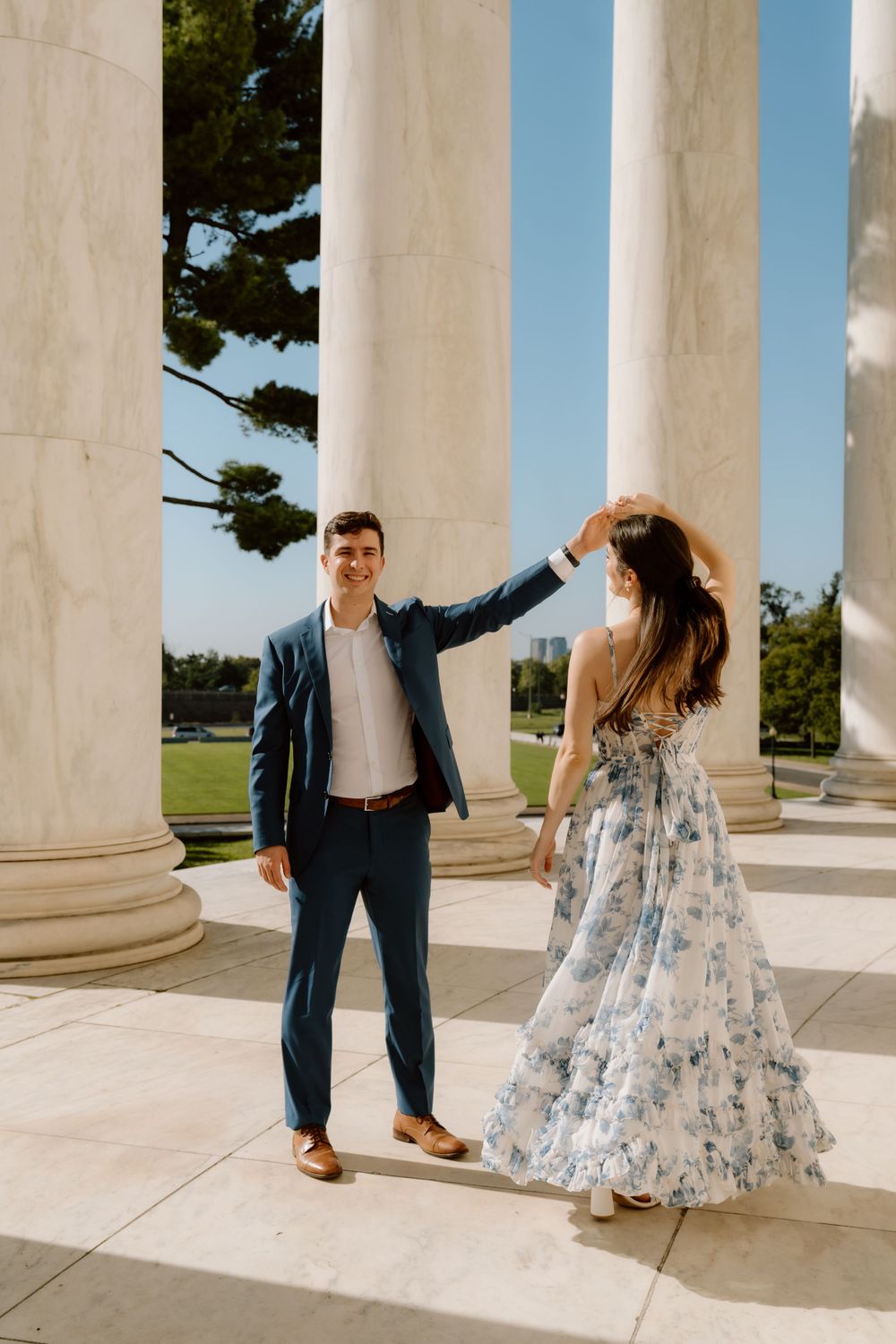 Two people dance and twirl together between the elegant white stone columns of the monuments in DC on a sunny day