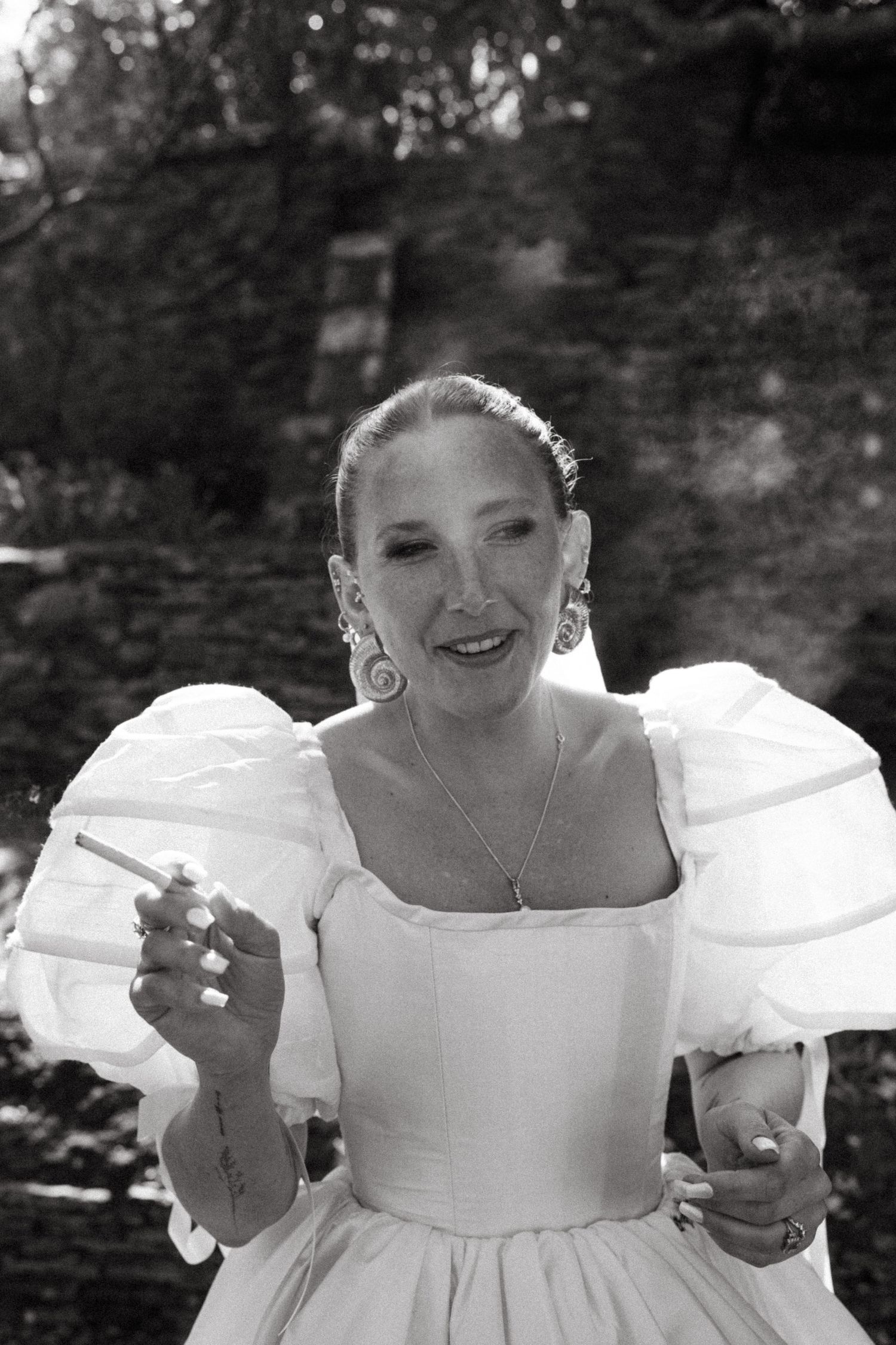 Black and white portrait of a person in a formal white dress with puff sleeves and statement earrings.