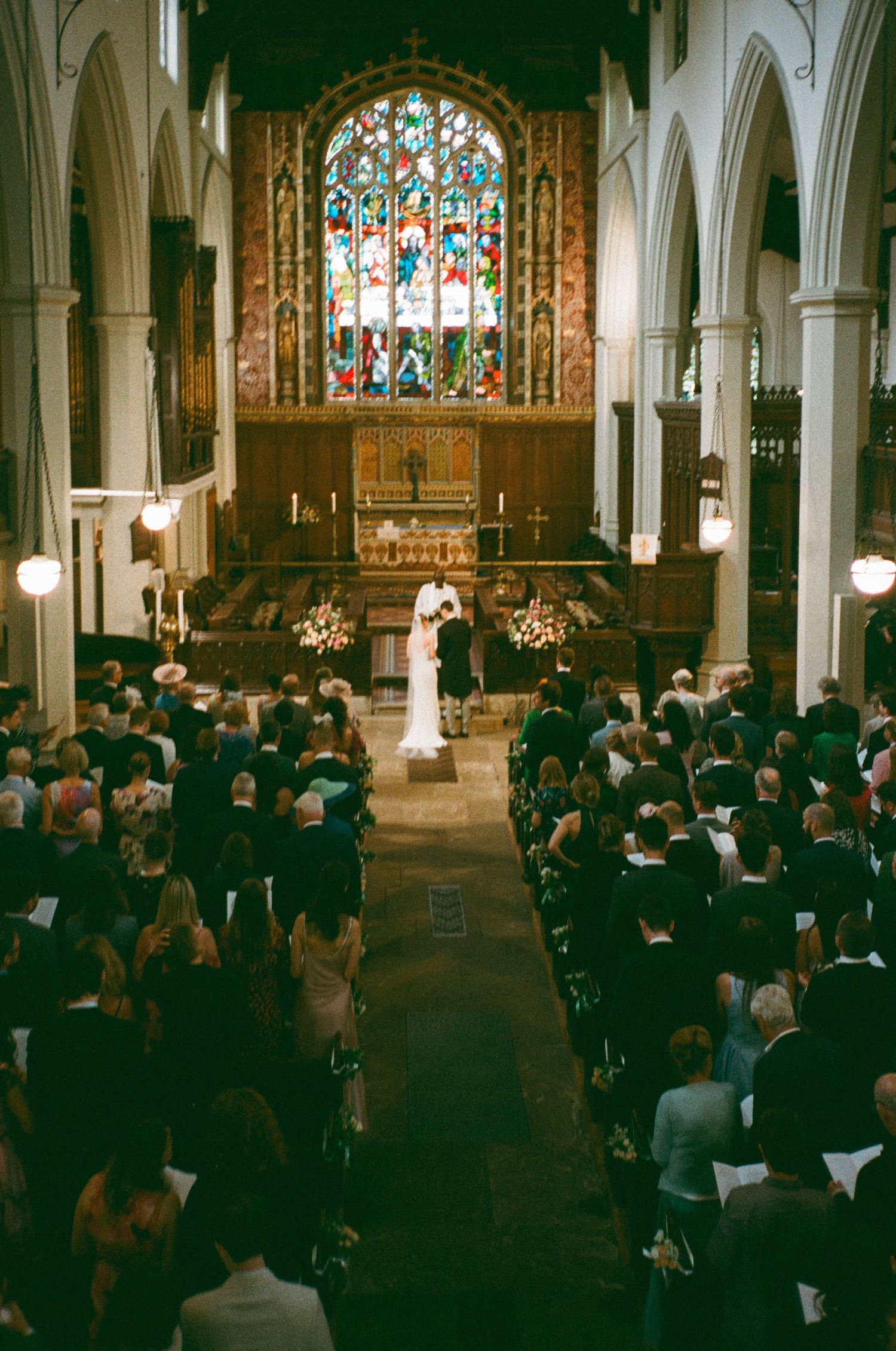A crowded church ceremony with stained glass windows and Gothic architecture filled with attendees in formal attire.
