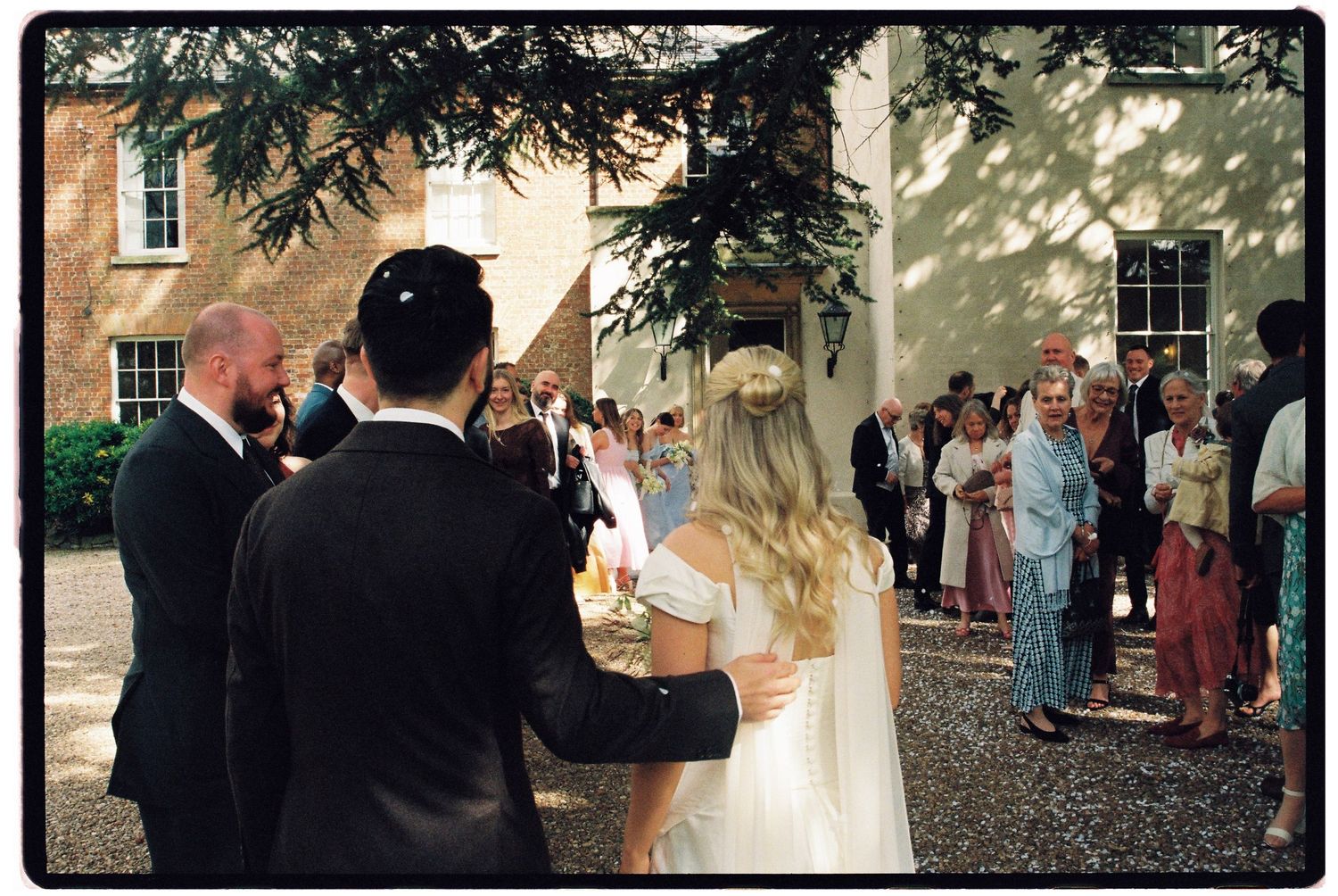 Bride and groom greeted by guests outside elegant brick venue during outdoor wedding reception ceremony.