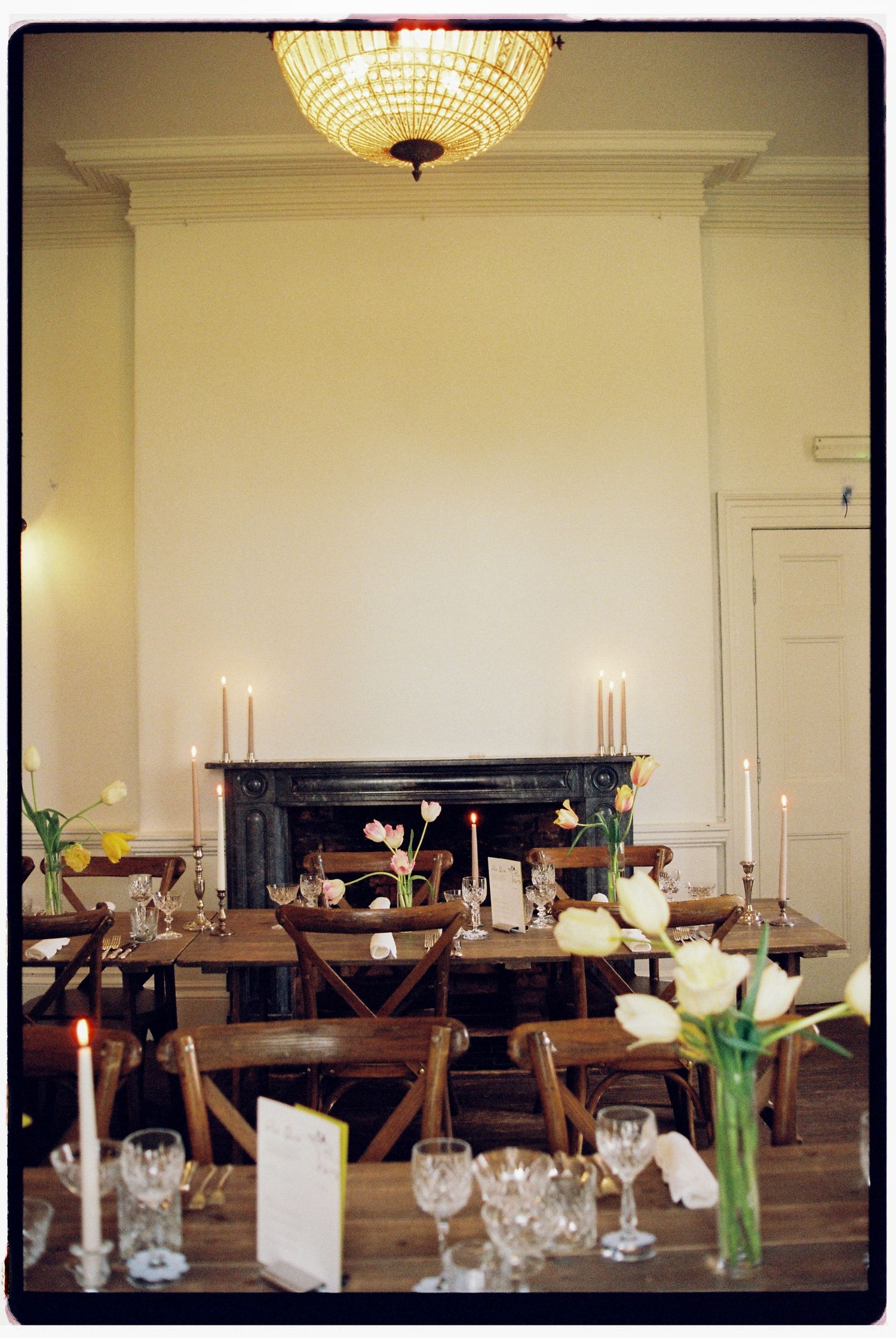 Elegant dining room with wooden tables, candles, tulip centerpieces, and a fireplace in a classic white interior.