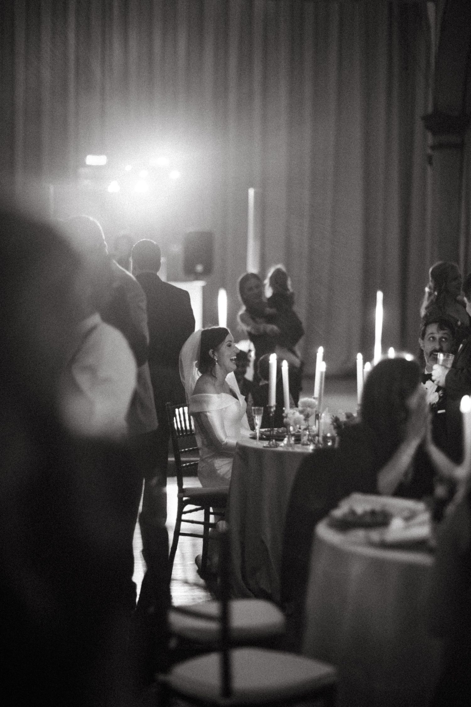 Black and white candid photo of an intimate wedding reception with candles and ambient lighting at elegant dinner setting.