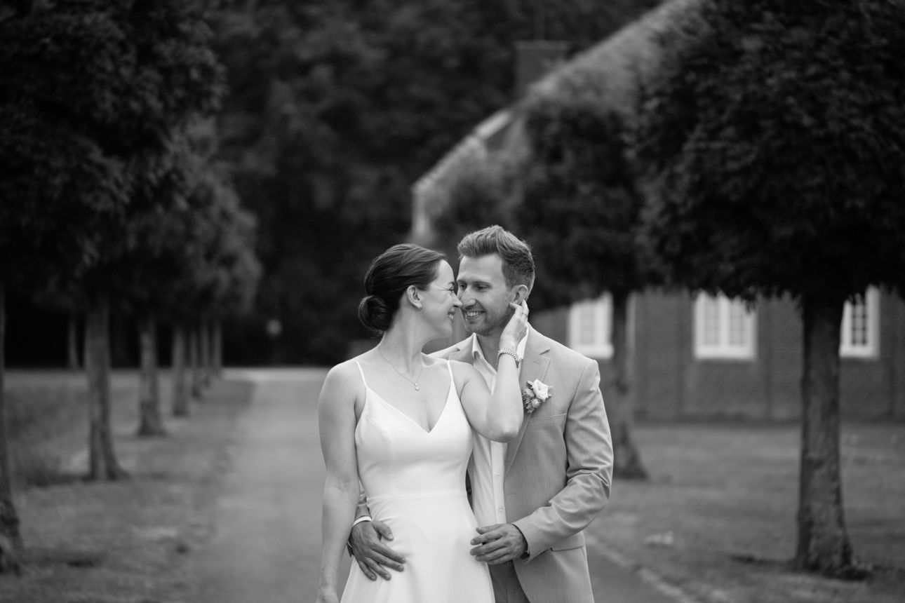 Black and white portrait of newlyweds sharing intimate moment by brick wall.
