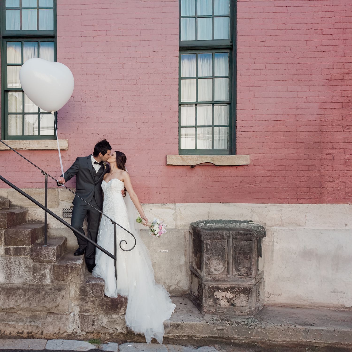 Romantic shot of couple on stone staircase holding white balloon against pink building, Suffolk wedding photography.