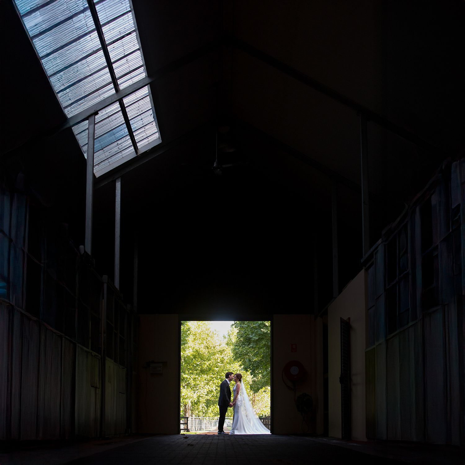 Bride and groom kissing in doorway of rustic dark barn with skylight, East Anglia wedding photographer.