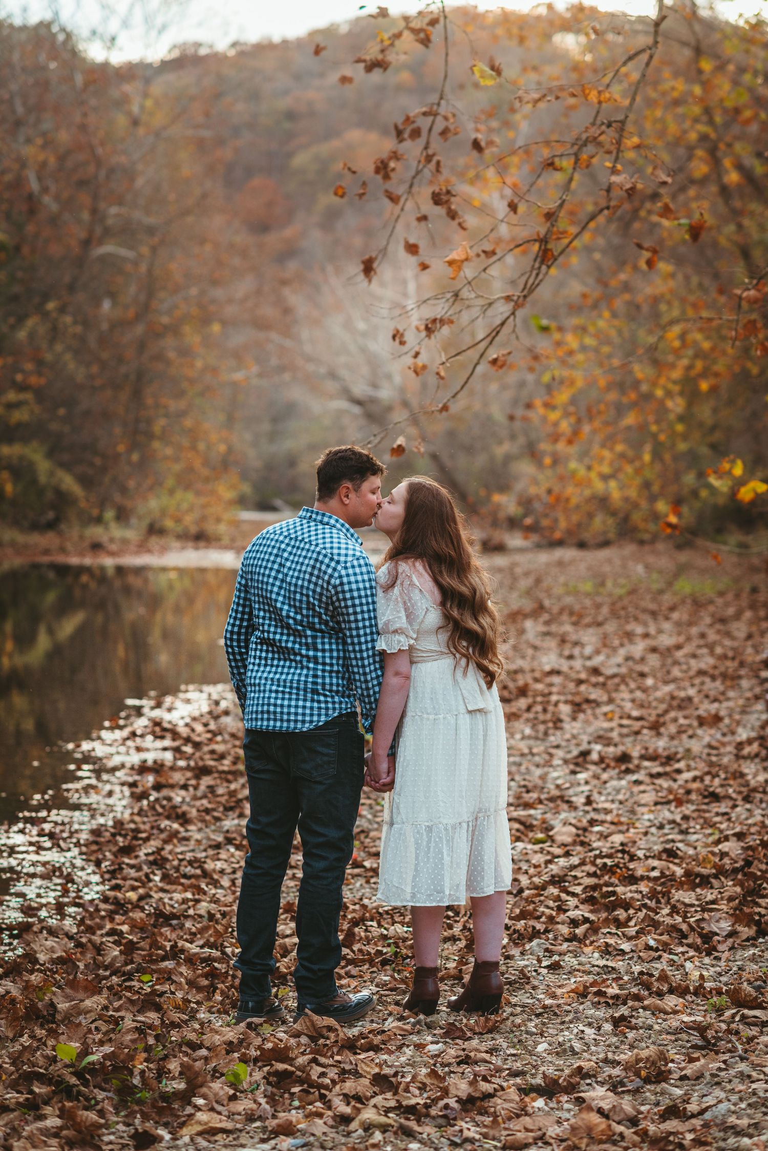 Autumn engagement photos with couple walking through fallen leaves by a lake.