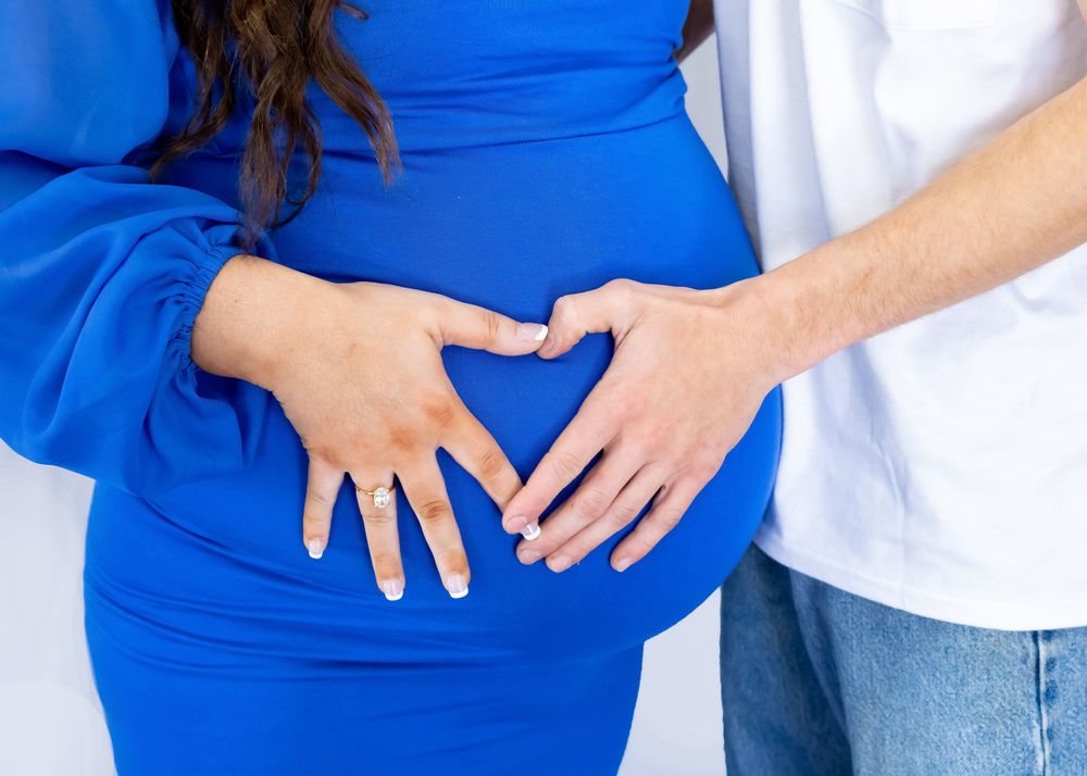 Close-up shots of hands cradling baby bump in bright blue maternity dress.