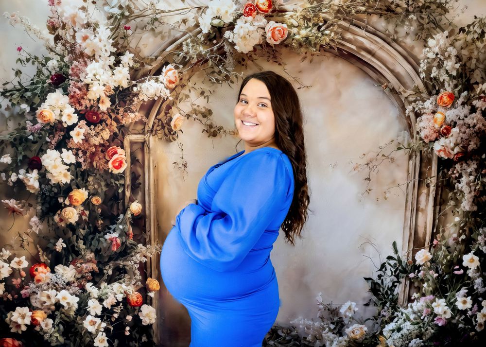 Maternity photography session with floral backdrop and flowing cobalt blue dress.