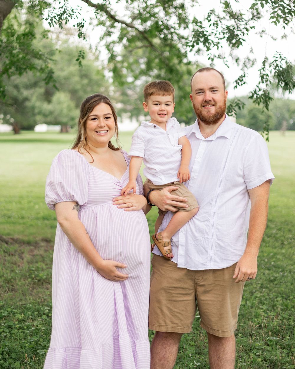 A casual outdoor family portrait in a green park setting.