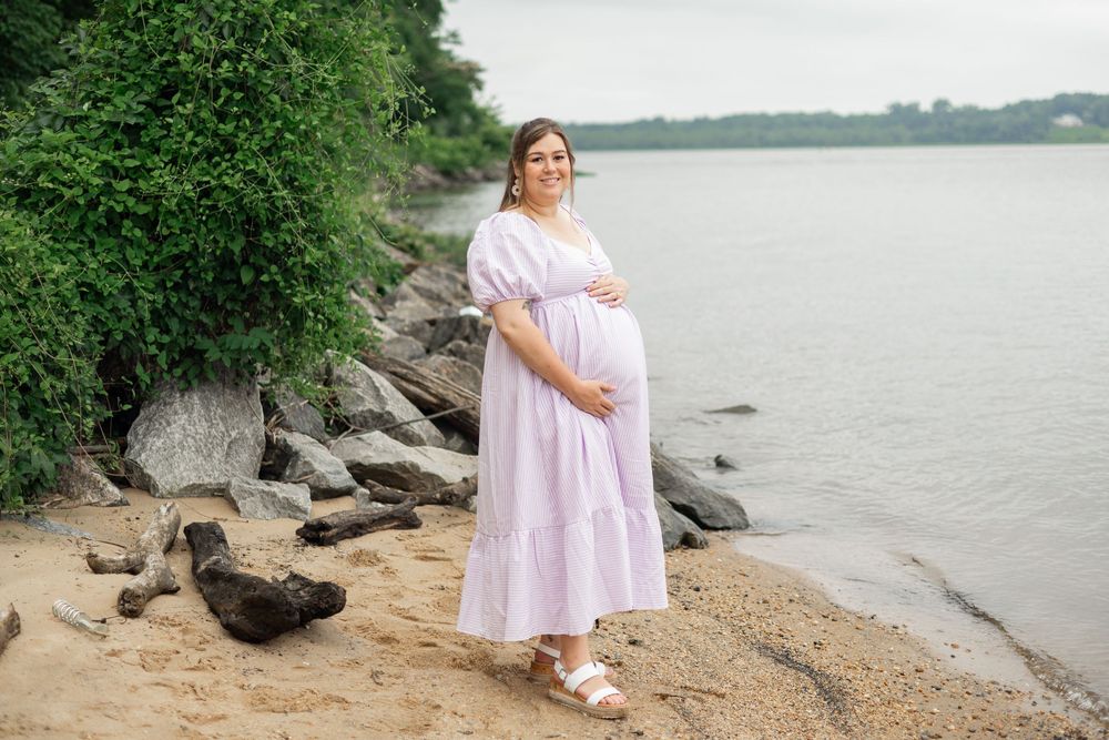 A maternity portrait on a rocky beach shore with water in the background.