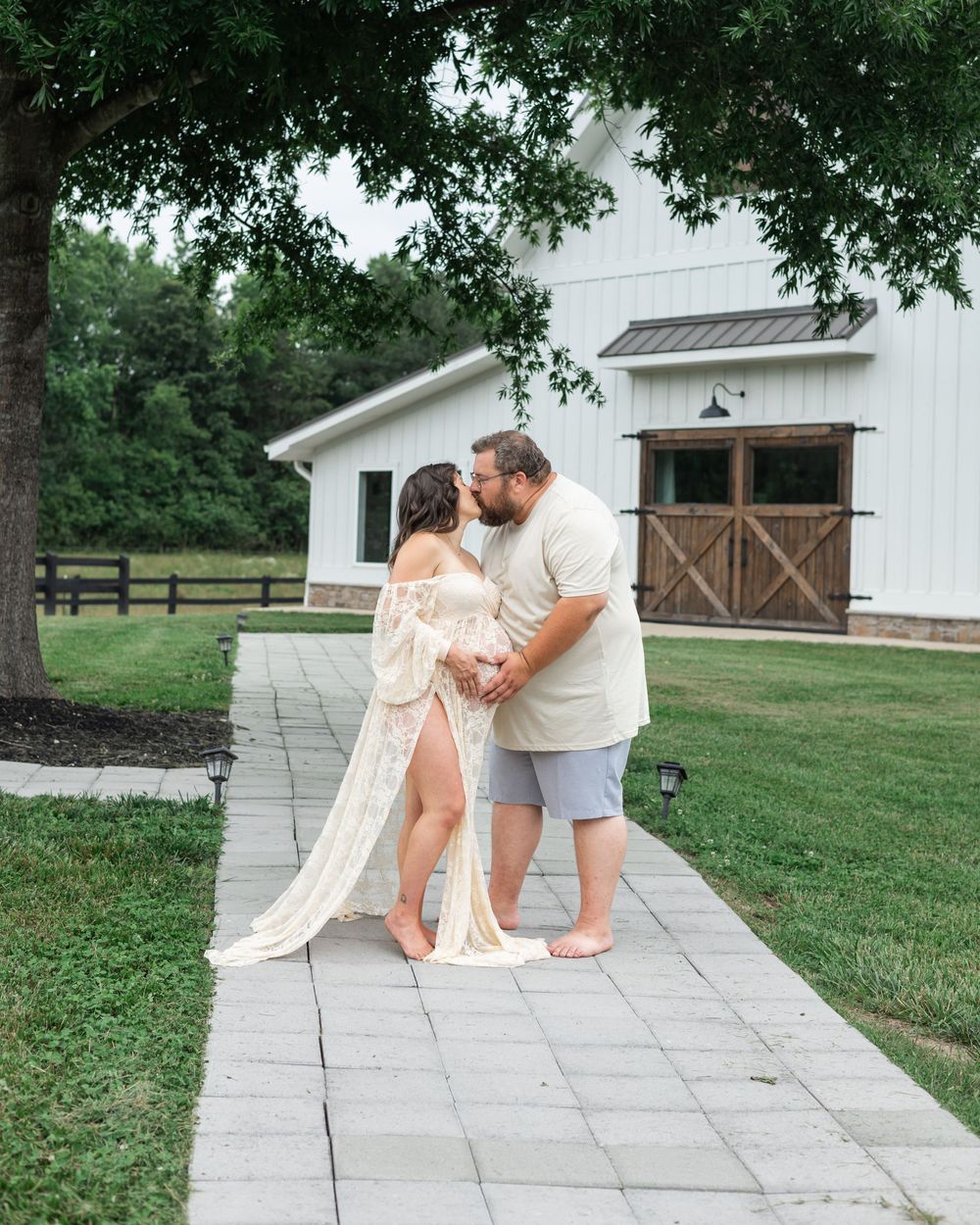 A romantic couple embraces on a stone pathway in front of a white barn.