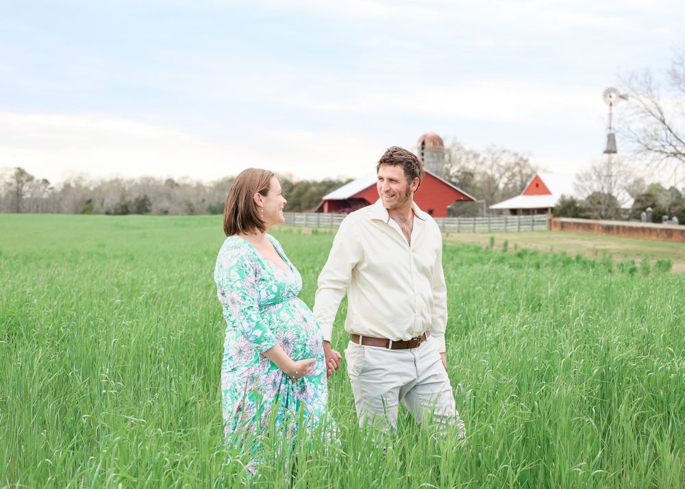 Couple walking through sunny spring meadow during outdoor maternity photoshoot.