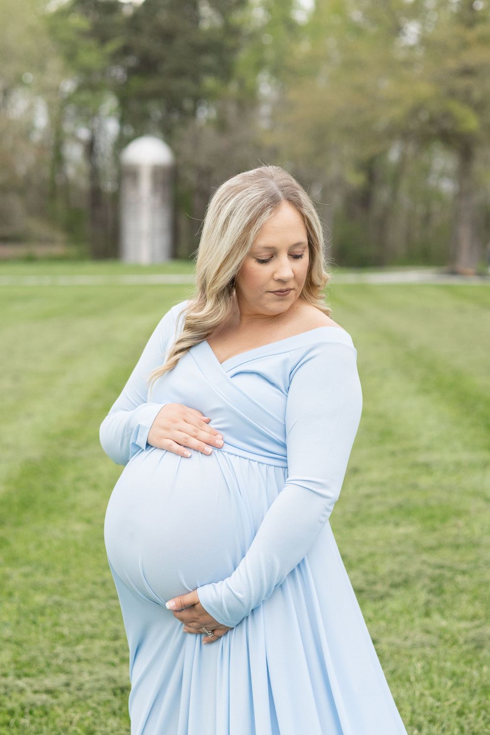 Maternity photography session in light blue dress on grassy field during golden hour.