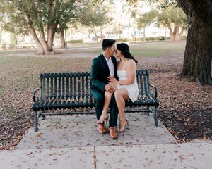 Couple sharing a romantic moment on a park bench surrounded by trees and autumn leaves.