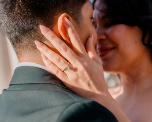 Close-up of bride touching grooms face showing diamond engagement ring, romantic wedding couple moment.