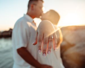 A close-up of an engagement ring with a couple kissing in soft sunset light.
