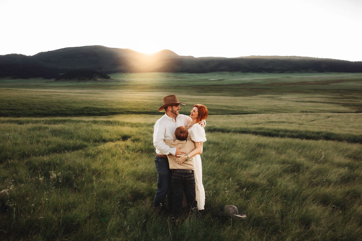 New Mexico family embracing at golden hour in a lush green meadow with Jemez mountains in the background.