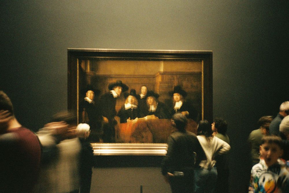 Visitors admiring Rembrandt's The Night Watch painting in a dimly lit museum gallery. Film Photography.