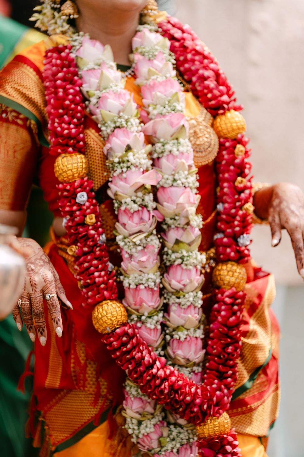 Indian bride wearing vibrant traditional floral garlands with pink lotus, red, and white flowers at a Hindu wedding ceremony.