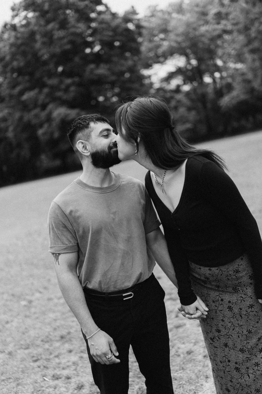 Black and white photo of a couple sharing a kiss outdoors in a park, holding hands romantically. Taken at Piedmont Park, Atlanta GA.