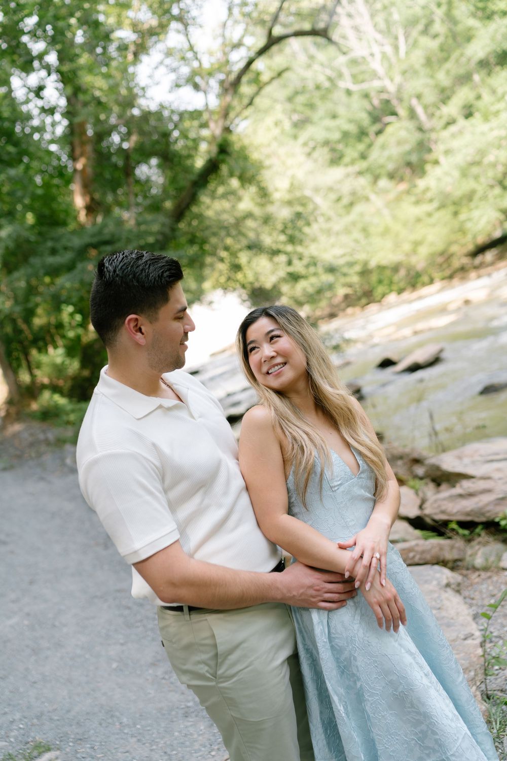 A couple embraces and smiles at each other on a scenic path surrounded by trees and rocks.