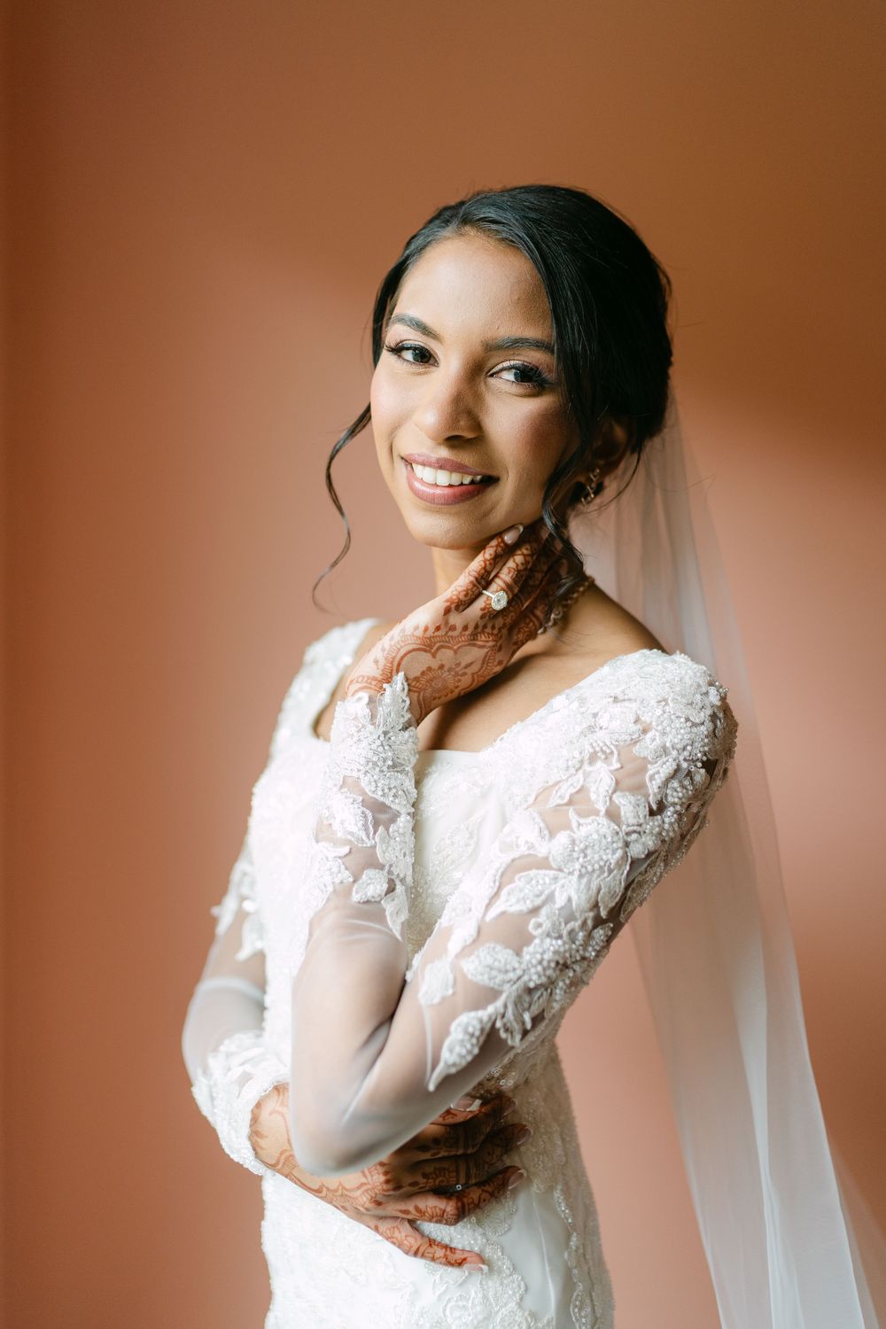 Bridal portrait series showing movement in flowing white lace wedding gown and veil against warm brown backdrop.