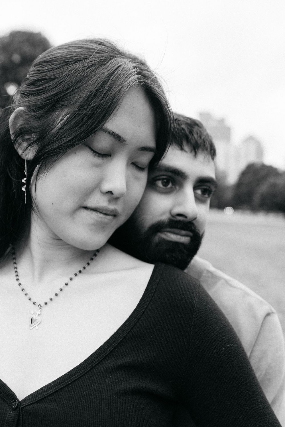 Black and white portrait of a couple, woman with closed eyes leaning on bearded man outdoors. Taken at Piedmont Park.