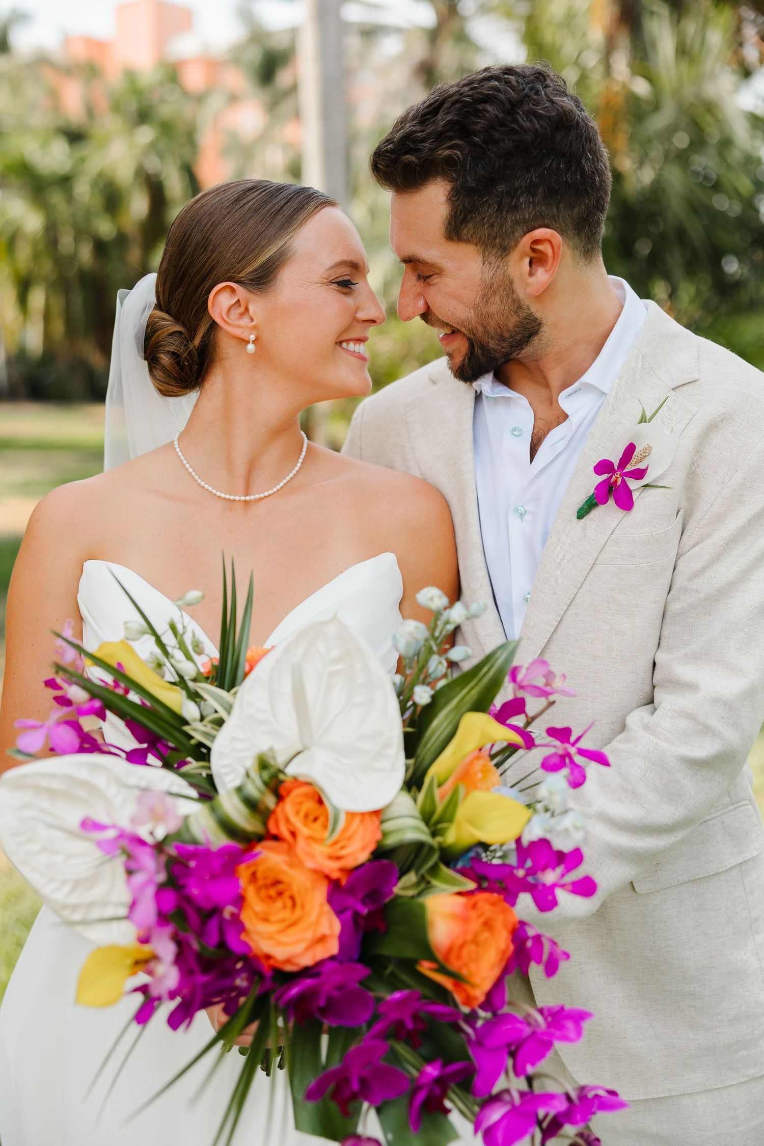 Bride and groom share a romantic moment holding a vibrant tropical bouquet of purple orchids and orange roses.