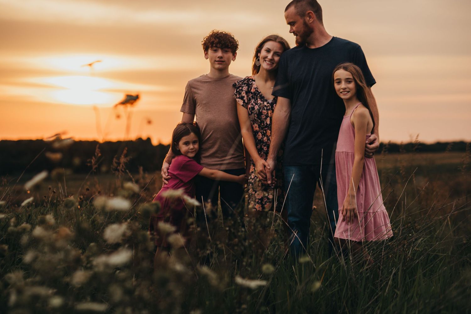 Family of five posing together in field during golden hour sunset.