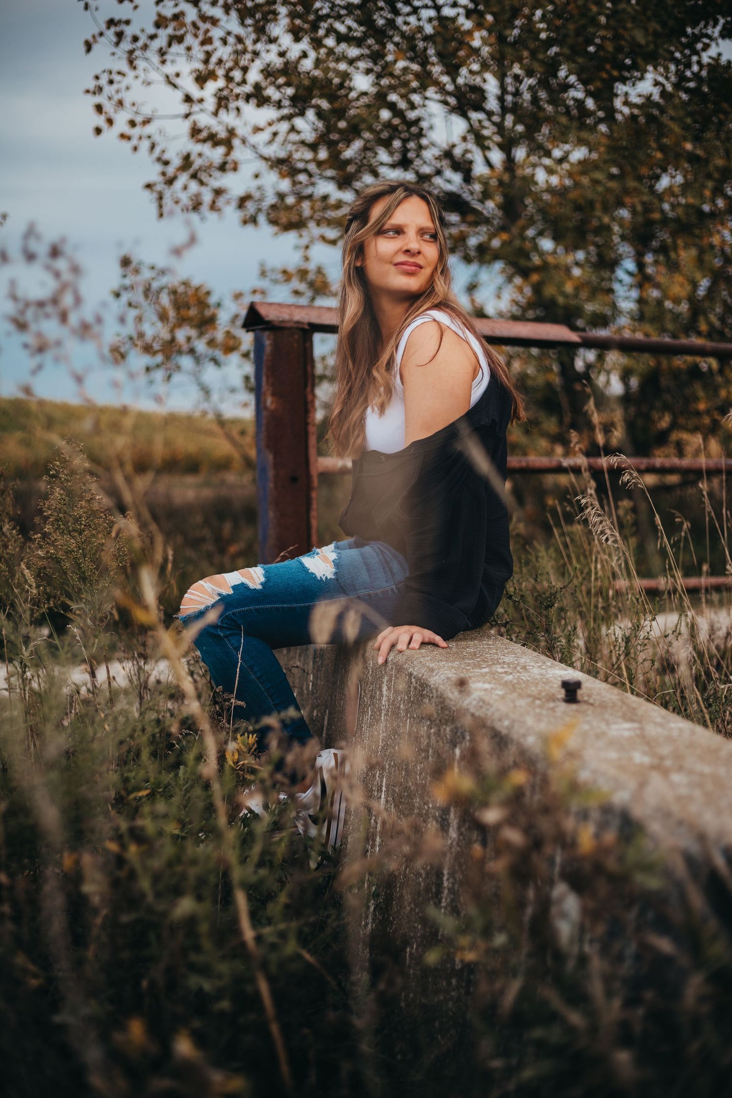 Woman in casual attire sitting on wooden fence post in rustic outdoor setting.
