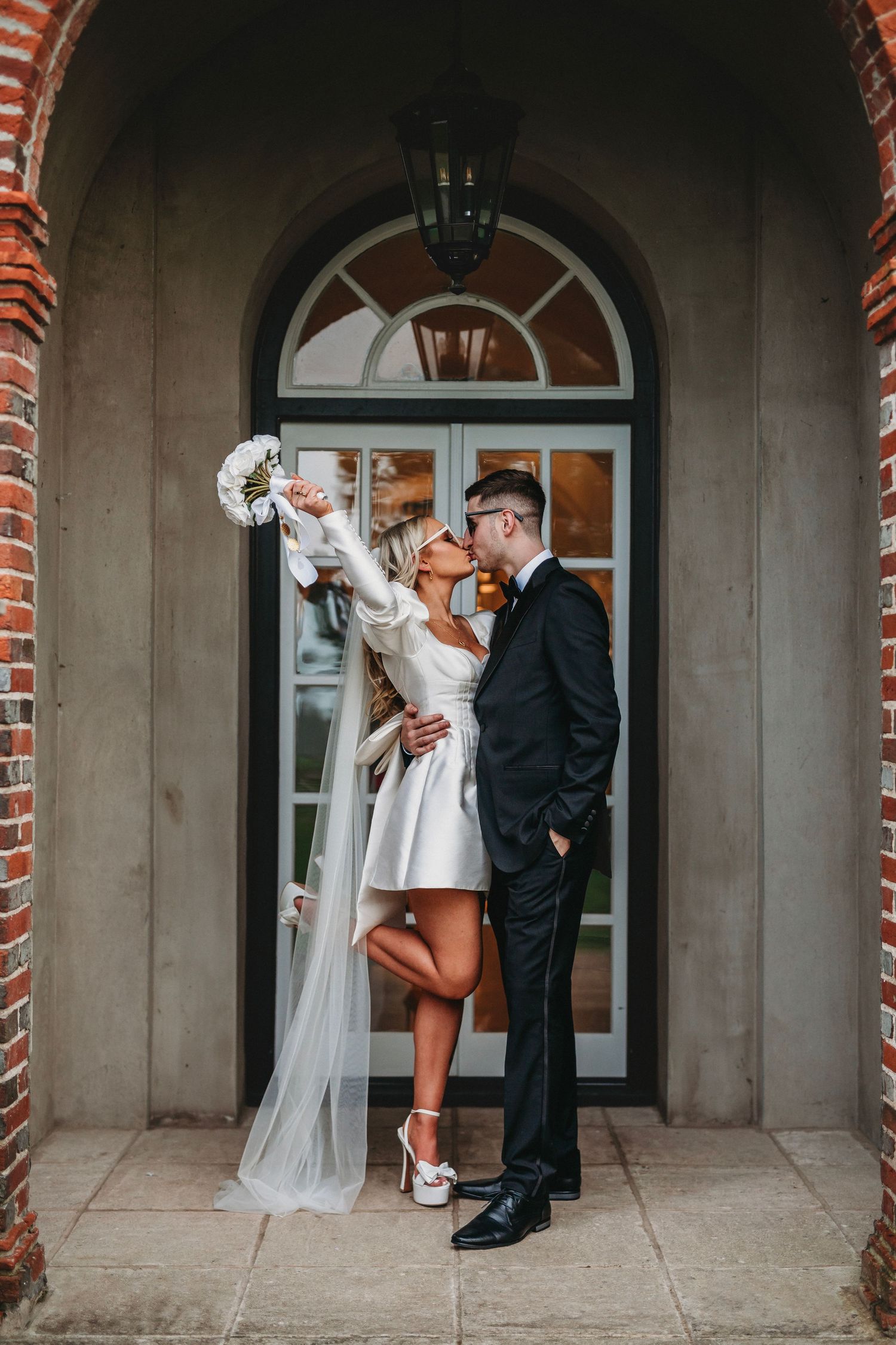 Wedding couple poses dramatically in an archway with red brick columns.