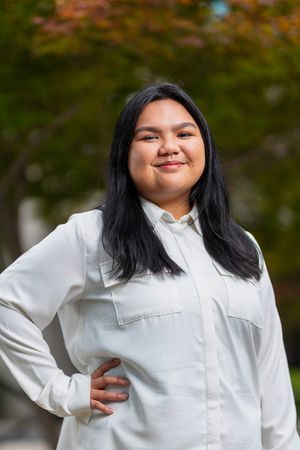 Portrait of person in white button-up shirt posing against autumn foliage background.