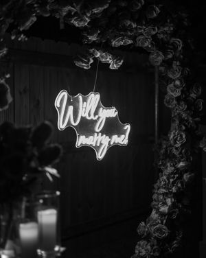 Black and white neon sign installation with romantic text and floral decor.