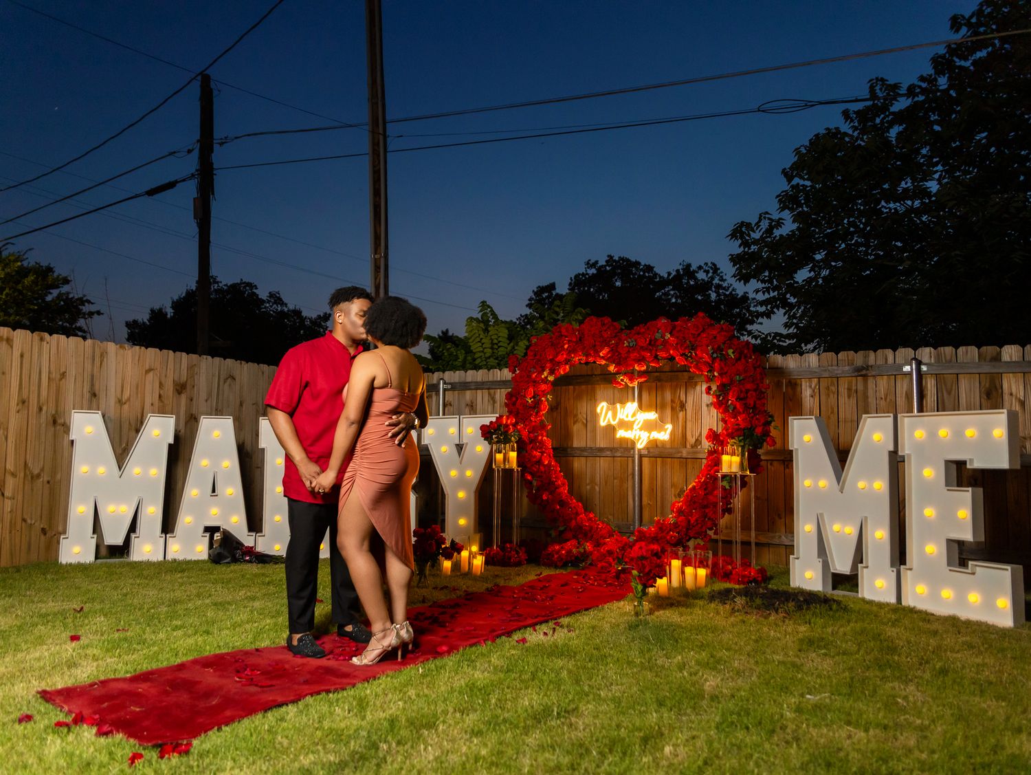 Large red letters spelling out 'MARRY ME' arranged outdoors with a romantic proposal setup.