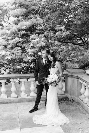 A romantic black and white wedding photo captured on stone steps surrounded by lush trees.
