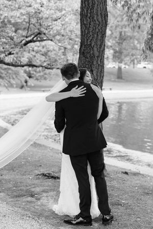 A romantic black and white wedding photo series showing a couple embracing by a lake with a flowing veil in the breeze.