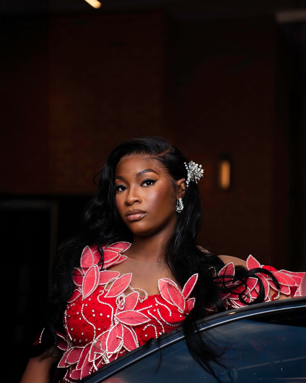A woman in a red ruffled dress poses elegantly on a dark couch during a glamour photoshoot.