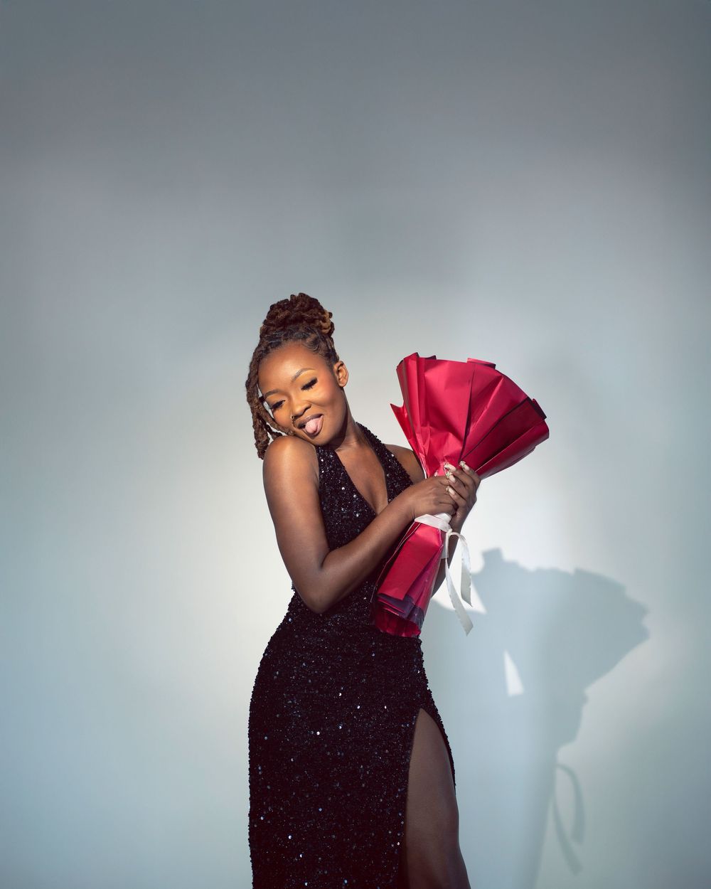 A dancer in a black sparkly dress strikes an elegant pose against a light background with dramatic shadows.