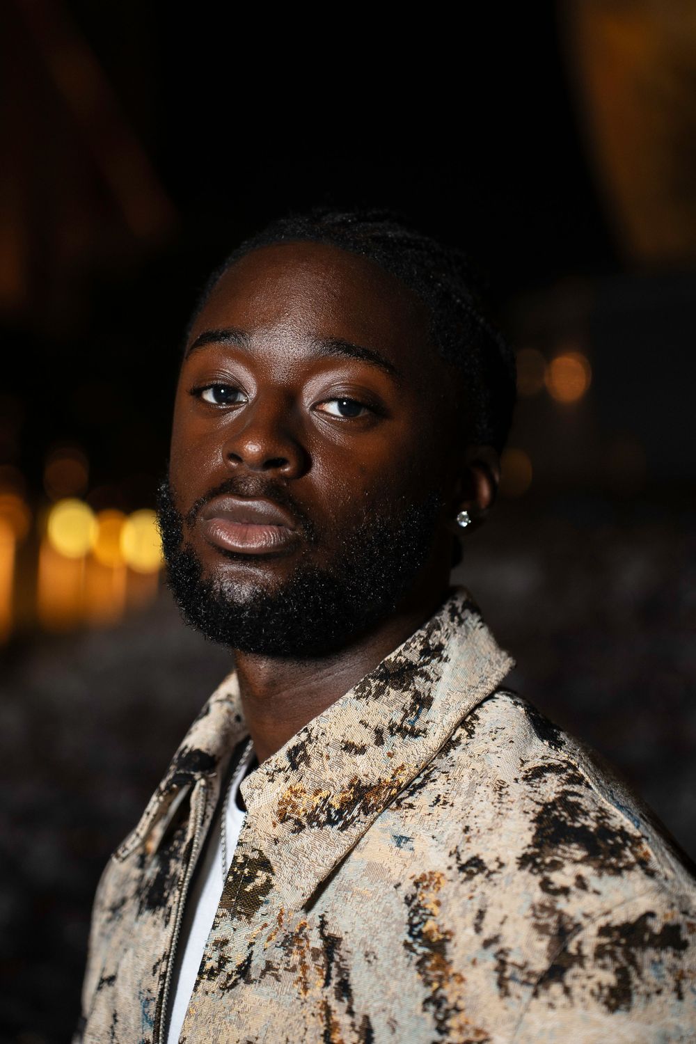 A person in a paint-splattered white jacket gazes upward against a dark background in a sequence of portraits.