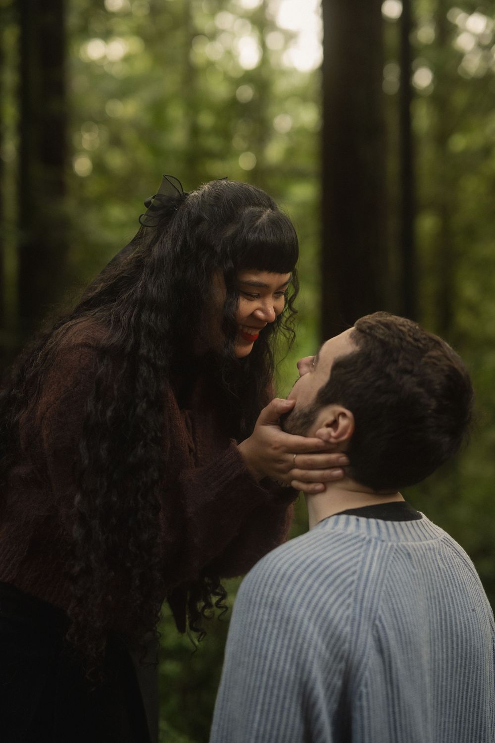 Two figures embrace in an intimate moment surrounded by sunlit forest trees.