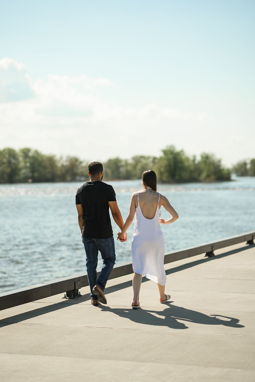A couple sits together on a waterfront dock during sunset, creating long shadows on the concrete surface.