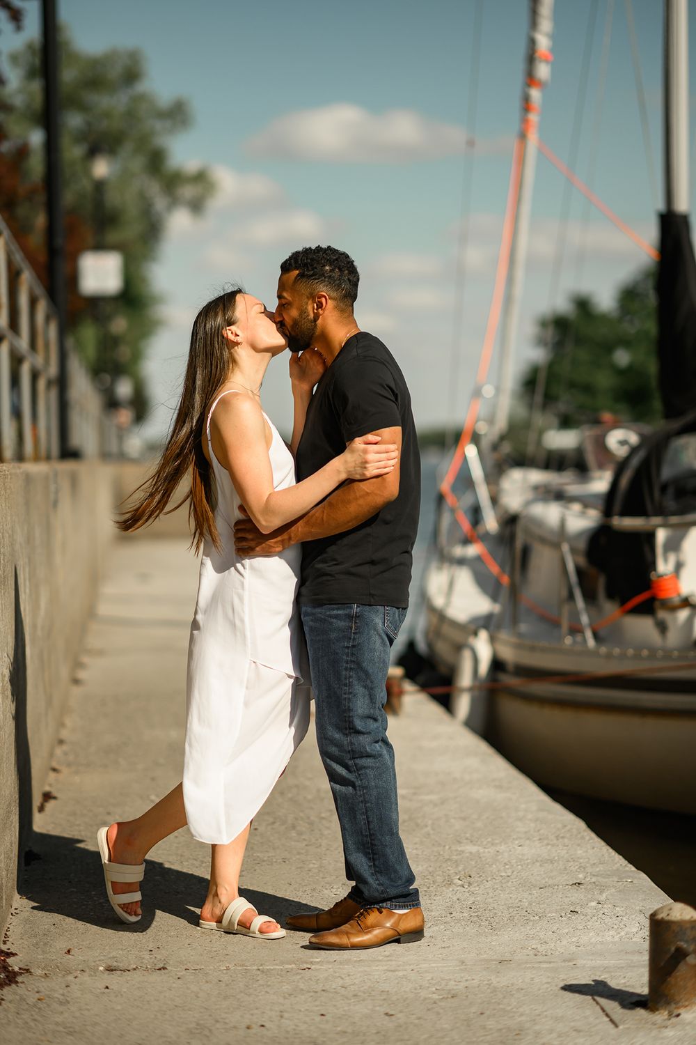 A couple shares tender moments on a dock with boats in the background during sunset.
