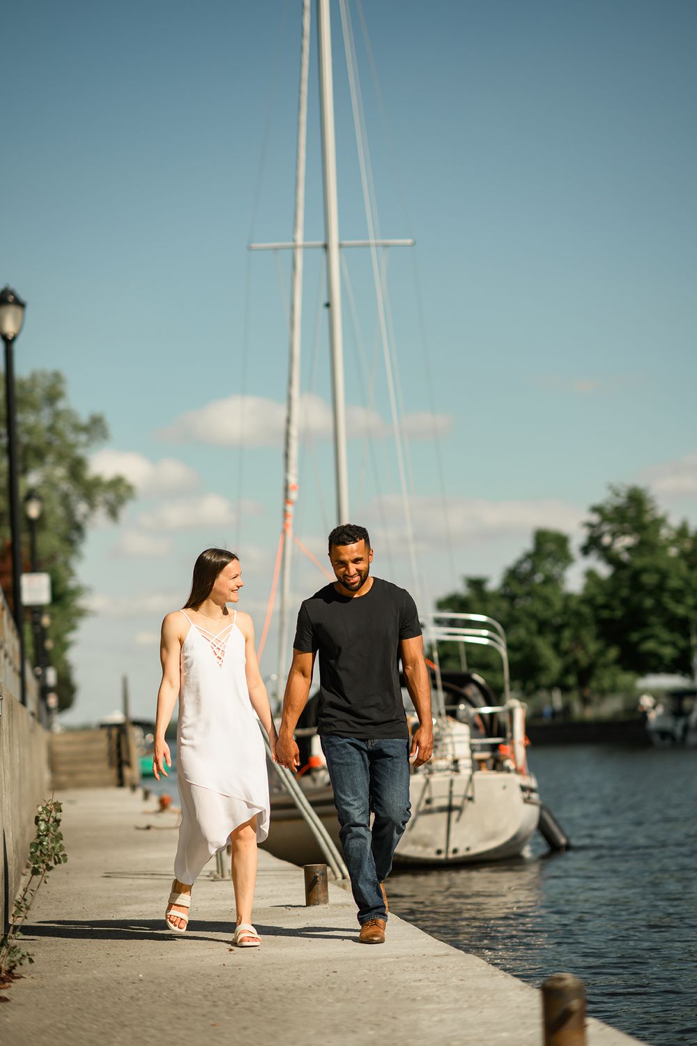 A couple walks along a wooden dock by sailboats on a sunny summer day, captured in a series of romantic photos.
