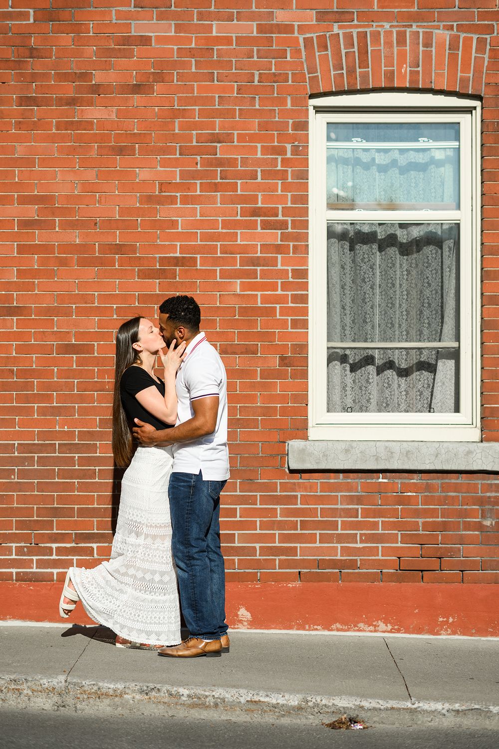 A romantic couple embraces against a red brick wall with white trimmed windows in a series of three connected photos.