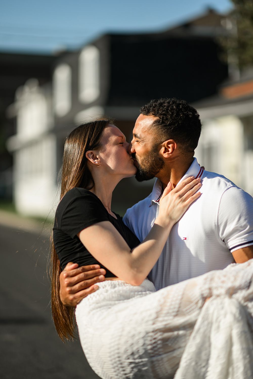 A romantic couple sharing a tender kiss while embracing outdoors on a sunny day.