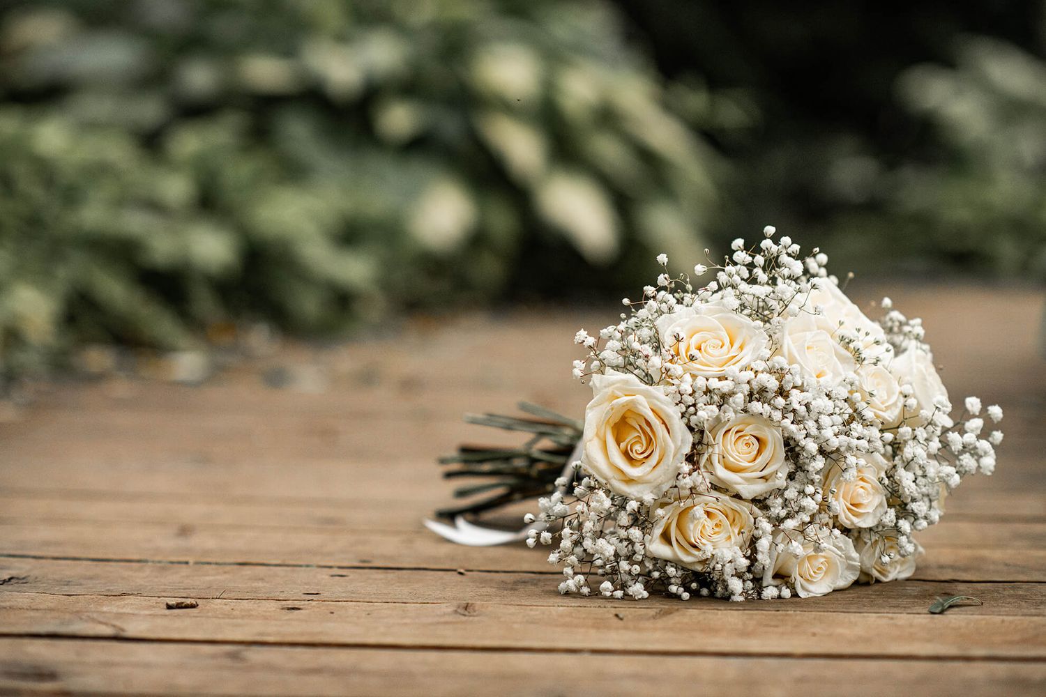 Delicate floral wedding arrangement with cream roses and baby's breath on wooden surface.